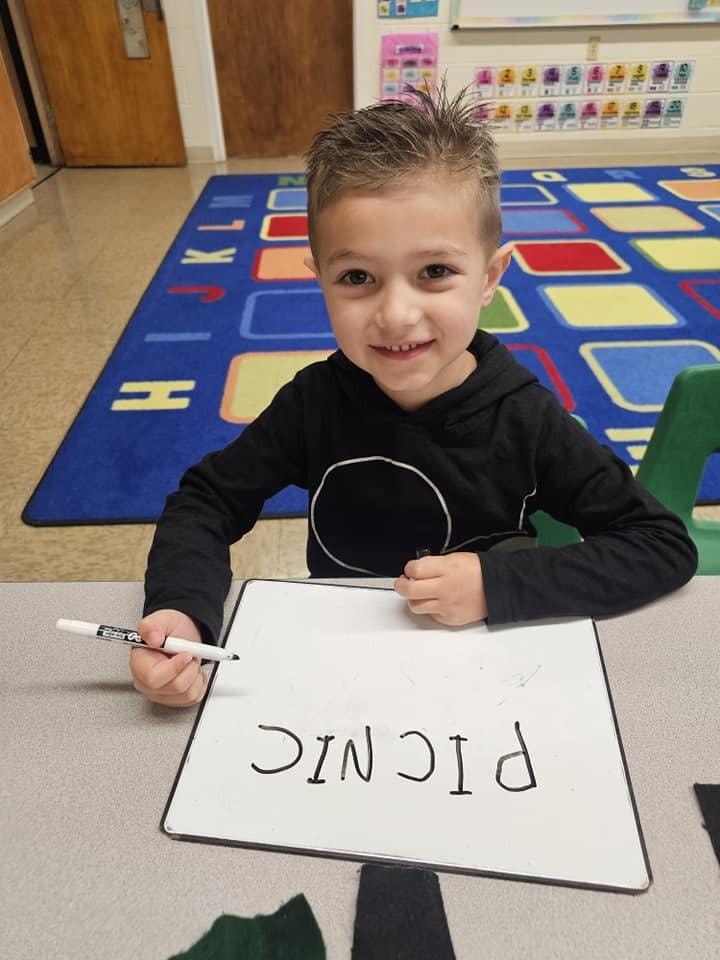 Young child holding handwritten sign in classroom